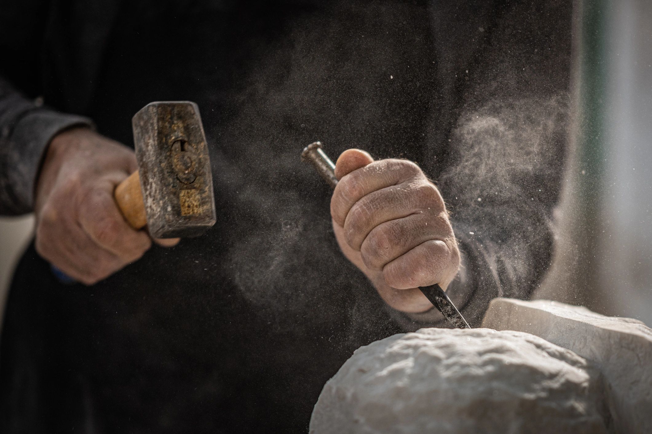 Hands shaping stone with hammer and chisel