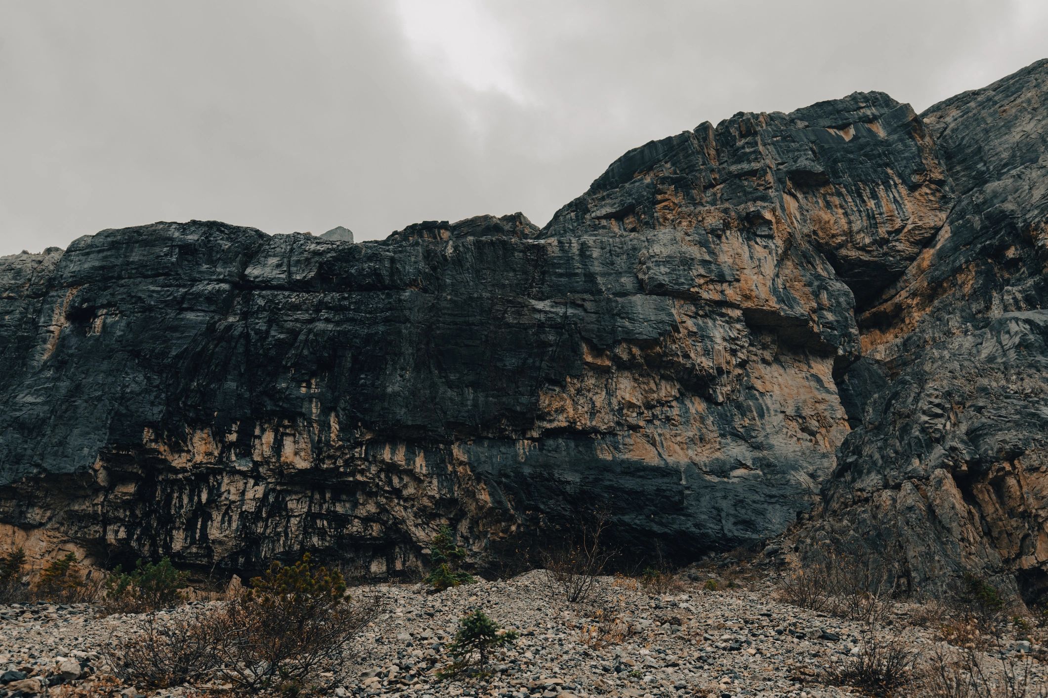 Rocky cliff face with scree slope under overcast sky